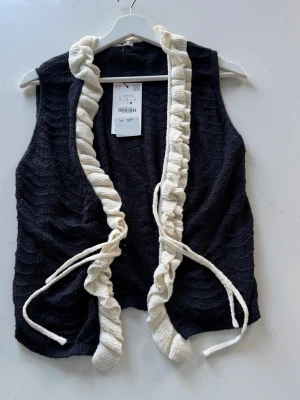 Svart väst med volangkant och knytband - Zara Stickad Väst – Aldrig använd med lapp kvar! 🏷️ Säljer denna superfina väst från Zara i storlek L. Marinblå med cremevita volangkanter – ett trendigt och feminint plagg som passar perfekt till både jeans och kjol! Plagget är helt oanvänt med original-lappen kvar, i absolut nyskick. 🔹 Märke: Zara  🔹 Storlek: L  🔹 Färg: Marinblå med cremevita detaljer  🔹 Detaljer: Öppen framsida med volangkanter och knytband  🔹 Skick: Nyskick – lapp kvar ✅  🔹 Nypris: 329 kr → Säljer för 179 kr Frågor? Skriv här