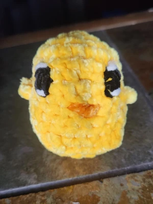 Gul virkad kycklingfigur - Söt handvirkad kyckling i mjukt gult garn med svarta och vita broderade ögon samt orange näbb. Perfekt som dekoration eller liten maskot. Rund och fluffig form, passar bra som present eller prydnad.