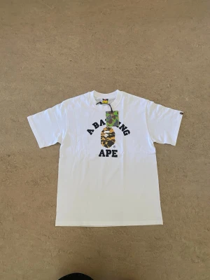 Bape T-Shirt - Säljer denna helt ny då den var för liten för mig, det är storlek M. Detta är en tröha från bape med klassiska camo loggan, perfekt för streetwear stilen nu till sommaren. Det är 100 bomull så den är väldigt luftig och skön! #streetwear #opium