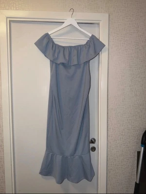 Ljusblå offshoulder långklänning - Snygg ljusblå långklänning med offshoulder och volangdetalj upptill samt nertill. Klänningen har en rak passform och är perfekt för sommarens tillfällen. Materialet känns mjukt och lätt. 