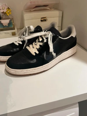 Svarta Polo Ralph Lauren sneakers - Snygga svarta sneakers från Polo Ralph Lauren med vita detaljer och vit sula. Skorna har klassisk låg profil, vita skosnören och Polo-logga på hälen. Materialet är en mix av läder och textil för en stilren look.