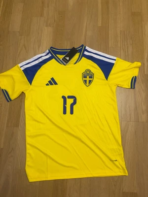 Sveriges vm tröja gyökeres M - Gul och blå matchtröja från Adidas för Sveriges landslag, med nummer 17 och namnet Gyökeres på ryggen. Tröjan har korta ärmar, blå detaljer på axlar och ärmslut samt landslagets emblem på bröstet. Tillverkad i lätt och ventilerande material.