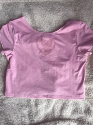 Rosa croppad topp från Dolly Style - Själer min  ljusrosa crop top från Dolly Style med korta ärmar och ett diskret hjärtmotiv framtill. väl använd men har inga fläckar eller liknande, rök och djur fritt hem. Storlek M