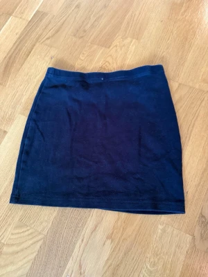 Svart kortkjol i bomull - En enkel och stilren svart kortkjol i mjukt bomullsmaterial. Kjolen har en rak passform och är perfekt att matcha med olika toppar för en clean look.