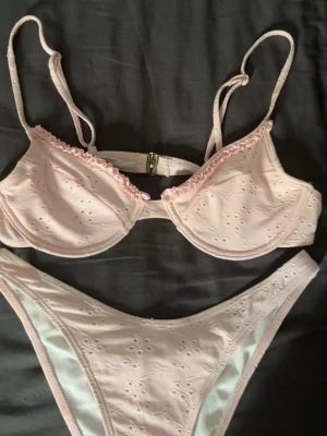 Ljusrosa bikini med volangdetalj - Supersöt ljusrosa bikini med små broderade blommor och volangkant på överdelen. Bikinin har justerbara axelband och bygel för extra stöd. Perfekt för sommarens strandhäng eller poolparty!