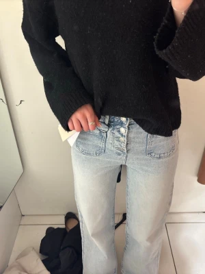 Ljusblå high waist jeans med knappar - Säljer ett par ljusblå jeans med hög midja och raka ben. Jeansen har flera silverfärgade knappar framtill och stora fickor både fram och bak. Klassisk denimlook i mjukt bomullsmaterial, perfekta till vardagsoutfiten.