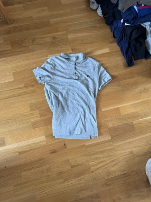 Grå pikétröja från Calvin Klein - Snygg grå pikétröja från Calvin Klein med klassisk krage och knappar framtill. Tröjan har korta ärmar och en broderad CK-logga på bröstet. Perfekt för en clean och stilren look.