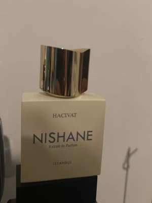 Nishane Hacivat Extrait de Parfum - Exklusiv parfym från Nishane, Hacivat Extrait de Parfum. Flaskan är fyrkantig och krämfärgad med en elegant, guldig och spegelblank kork. Märket och doftnamnet är tryckta i svart på framsidan. Perfekt för dig som gillar lyxiga dofter. 50 ml flaska mängden som är kvar är vid extrait de parfum texten