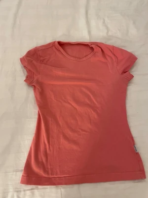 Korallrosa t-shirt i bomull - En enkel och snygg korallrosa/aprikos rosa t-shirt med rund hals och korta ärmar. Modellen är figurnära och passar perfekt till jeans eller shorts. Tillverkad i mjuk bomull för skön komfort hela dagen.