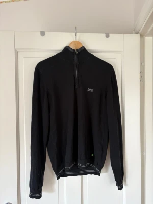Svart halfzip-tröja från BOSS - Snygg svart långärmad tröja från BOSS med halfzip och hög krage. Tröjan har diskret BOSS-logga på bröstet och ribbade muddar vid ärmslut och nederkant. 
