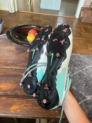 Nike Phantom GT2 turkosa fotbollsskor - Säljer ett par Nike Phantom GT2 fotbollsskor i turkos och vitt med svarta detaljer. Skorna har snörning, syntetmaterial och dobbar för spel på gräs. Swoosh-logga på sidan och textdetaljer. Perfekta för dig som vill ha kontroll och stil på planen. Inga stora skador på skorna, tvättas noga innan förpackning.😊