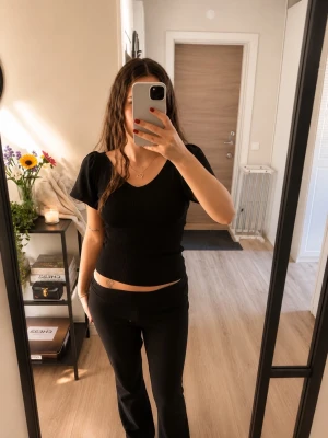 Svart ribbad topp med puffärm - Trendig svart ribbad topp med korta puffärmar och v-ringning. Toppen har en snygg öppen rygg med knytband upptill för extra detalj. Perfekt att styla med både jeans och kjol.
