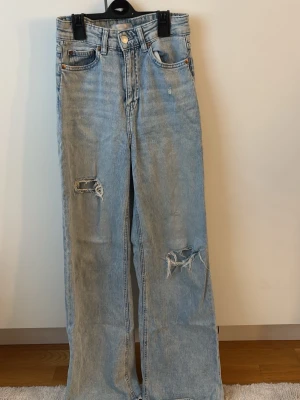 Jeans med slitning - Säljer ett par ljusblå jeans från H&M i storlek 34. Jeansen har raka ben och snygga slitningar på båda benen för en trendig look. Gåva vid köp!🎁