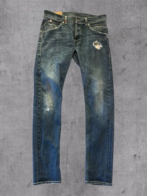 DonDup jeans - Säljer ett par blå jeans med slitningar och hål på låret och knät. Jeansen har raka ben, klassisk femficksmodell och kontrastsömmar. Perfekta för dig som gillar en avslappnad och trendig stil.