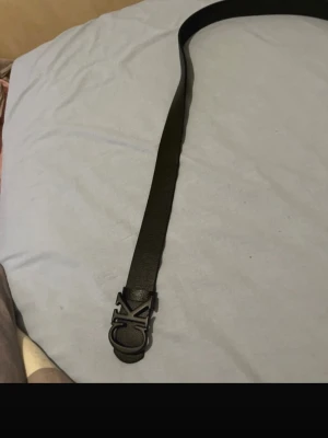 Svart Calvin Klein läderbälte - Snyggt svart bälte från Calvin Klein i äkta läder med en stilren metallspänne där CK-loggan syns tydligt. Perfekt accessoar för att lyfta din outfit med en clean och modern touch.