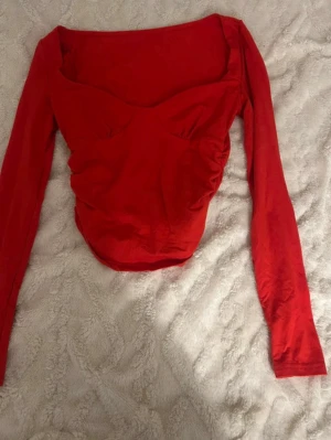 Röd långärmad topp med sweetheart-urringning - Snygg röd topp med lång ärm och en formad sweetheart-urringning. Toppens passform är tight och den har en feminin siluett som framhäver figuren. Perfekt att matcha med jeans eller kjol för en trendig look.