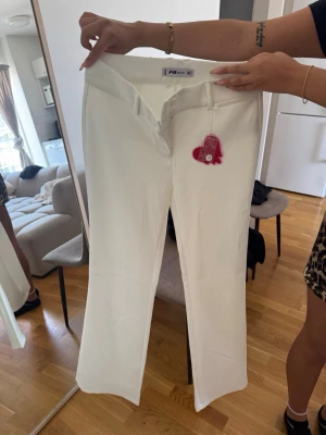 Vita raka jeans från Fila - Säljer ett par vita jeans från Fila med rak passform och bälteshällor. Jeansen har en enkel design och en liten rosa hjärtformad tag framtill. Perfekta för dig som gillar stilrena och fräscha plagg.