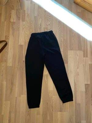 Svarta mjukisbyxor med resår - Säljer ett par svarta mjukisbyxor med resår i midjan och muddar vid bensluten. Perfekta för chill dagar hemma eller när du vill ha det bekvämt. Klassisk rak passform och mjukt material som känns skönt mot huden.