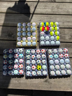 Samling golfbollar med olika mönster - Stor samling golfbollar med olika färger och mönster, bland annat bollar med fotbollsmönster, randiga och flerfärgade varianter. Perfekt för dig som vill ha unika golfbollar på banan eller samla på roliga designer.