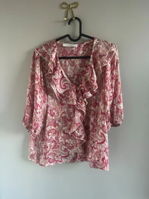 Paisleymönstrad blus från Sisters Point - Paisleymönstrad blus i rosa och vitt från Sisters Point. Blusen har volangdetaljer längs ringningen och framtill samt trekvartsärm. Tillverkad i ett lätt och luftigt material som ger en avslappnad men ändå chic look.