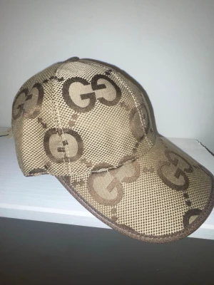 Beige keps från Gucci med GG-mönster - Säljer en beige keps från Gucci med det klassiska GG-mönstret i brunt. Kepsen har böjd skärm och är tillverkad i ett slitstarkt tygmaterial. Perfekt för dig som vill ha en stilren accessoar med lyxig känsla.