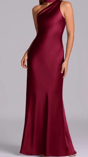 Vinröd oneshoulder långklänning - Elegant vinröd långklänning i satinliknande material med oneshoulder-design. Klänningen har en figurnära passform och slät yta som ger en lyxig känsla. Perfekt för dig som vill sticka ut med en stilren och modern look.