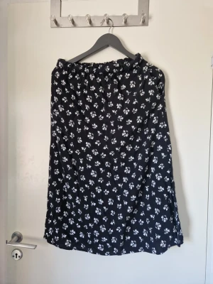 Svart blommig kjol - Blommig kjol från Lager 157 i storlek S ( kan passa någon som vanligtvis har S/M också ) med slits och fickor på vardera sida. Går ner till knäna på mig som är 168. Eftersom katt finns i hemmet och plagget är svart så finns det synliga katthår på den men det brukar gå bort lätt i antingen tvätten eller med hjälp av en klädroller.