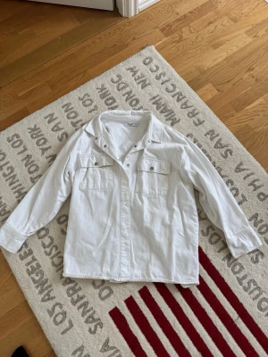 Vit oversize jeansjacka från NA-KD – stl 38 - Vit oversize jeansjacka från NA-KD i storlek 38. Jackan har en avslappnad passform och är perfekt att bära över både klänningar, jeans och andra vardagsoutfits. Använd men i fint skick. Den har en svag fläck, vilket syns på bilderna, men den påverkar inte helhetsintrycket nämnvärt. Ett stilrent och tidlöst plagg som passar året om.