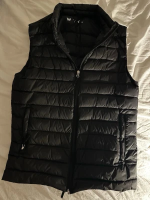 Svart dunväst från WYTE - Snygg svart dunväst från WYTE med quiltad design och hög krage. Bra skick och säljs nu för den inte används längre. Köptes för 250kr och säljs nu för 100kr. Kontakta mig om du har frågor.
