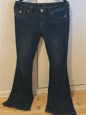 Mörkblå bootcut jeans True Religion - Snygga mörkblå bootcut jeans från True Religion med klassiska kontrastsömmar och dekorativa fickor bak. Jeansen har låg midja, fem fickor och silverfärgade knappar. Perfekta för dig som gillar en retroinspirerad look.  Säljs då de är förstora, pris går att diskutera 