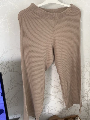 Beige ribbade leggings - Säljer ett par beige ribbade leggings med hög midja och stretchigt material. De har en bred linning och är tillverkade i mjuk, stickad kvalitet som känns skön mot huden. Perfekta för en chill och avslappnad stil.
