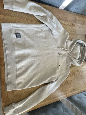 Beige hoodie från Morris  - Beige hoodie från Morris med klassisk huva och dragsnören. Mjuk bomullsblandning, ribbade muddar och diskret logotyp på bröstet. Patch med Morris -märke vid nederkanten. Perfekt för en avslappnad och stilren look. Inga defekter passar nån runt 175. Skriv vid minsta intresse🙌🙌🤗🤗