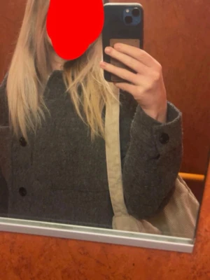 Grå ullmix cardiganjacka - Snygg grå cardiganjacka i ullmix med stora framfickor och knappar framtill. Jackan har en rak, boxig passform och klassisk krage. Perfekt att slänga över en hoodie eller t-shirt för en chill look.