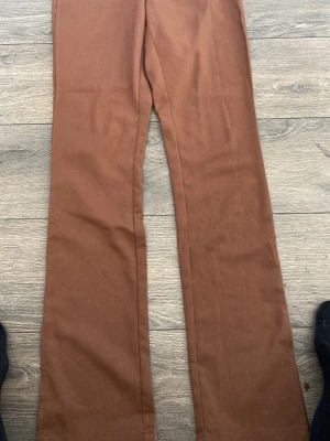 Bruna utsvängda byxor - Snygga bruna byxor med utsvängda ben och hög midja. Byxorna har en enkel design utan synliga fickor eller detaljer och är tillverkade i ett mjukt tyg som ger en skön känsla. Perfekta för dig som gillar en retroinspirerad look.