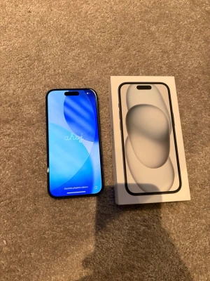iPhone 15 svart med box - Säljer en svart iPhone 15 från Apple med box. Mobilen har en stilren design med rundade hörn, två kameror på baksidan och en skärm med Dynamic Island. Materialet är glas och aluminium, vilket ger en premiumkänsla. Perfekt för dig som vill ha senaste modellen.