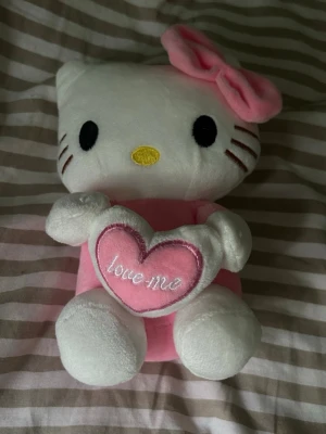 Hello Kitty gosedjur med hjärta - Hello Kitty gosedjur i vit och rosa. Den har en stor rosa rosett på huvudet och håller ett rosa hjärta med texten 'love me' broderat på. Perfekt som present eller dekoration💕