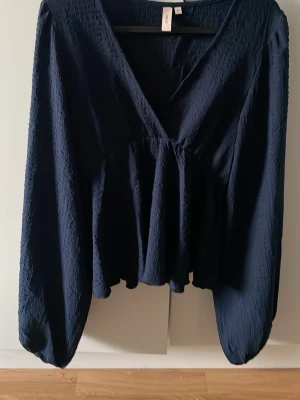 Mörkblå v-ringad blus från Nelly  - Snygg mörkblå blus från Nelly med v-ringning och långärmad design. Blusen har en lätt rynkad struktur i tyget och är aldrig använd