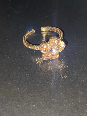 Isa Ring Crystal guldpläterad - Caroline Svedbom - Trendig ring i guldplätering med tre stora, klara kristaller i olika former framtill. Ringen har en öppen design som gör den justerbar och bandet är dekorerat med ett subtilt mönster. Perfekt för dig som vill ha ett statement-smycke med extra bling.
