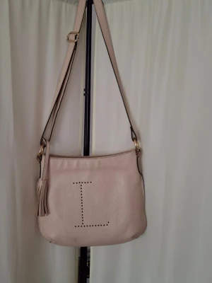 LOXWOOD beige axelväska med tofsdetalj - Detta är en klassisk beige fransk handväska fröm LOXWOOD (m9dell Le Cabas Parisien). Höjd-29cm Bredd-33cm Djup-7-9cm. Snygg beige axelväska från mjukt skinn. Baksidan har en praktisk ficka med dragkedja. Perfekt för dig som gillar stilrena accessoarer.