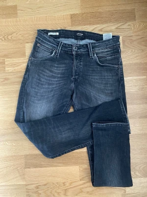 Mörkgrå slim fit jeans från Jack & Jones - Snygga mörkgrå slim fit jeans från Jack & Jones med klassisk femficksdesign och subtila slitningar framtill. 31/30