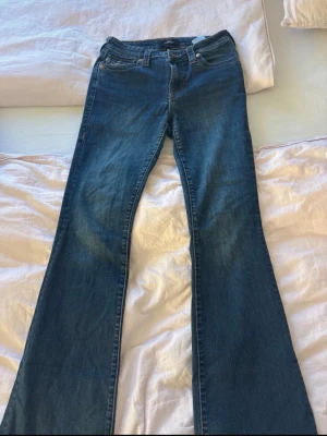 Blå bootcut jeans från True Religion - Säljer ett par blå bootcut jeans från True Religion med klassiska kontrastsömmar och snygga fickdetaljer bak. Jeansen har låg midja och är tillverkade i mjuk denim med stretch. Perfekta för dig som gillar en avslappnad men trendig look. Köpta kör 1300