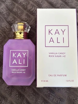 Kayali Vanilla Candy Rock Sugar 42 parfym - Kayali Vanilla Candy Rock Sugar 42 Eau de Parfum i en snygg lila glasflaska med gulddetaljer och kristallin kork. Flaskan rymmer 30 ml och har en modern, kantig design. Doften är söt och vaniljig, perfekt för dig som gillar gourmand-parfymer.Spreyad engast 1 gång för bara lukta