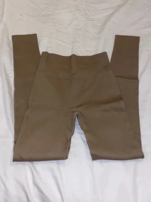 Ribbade bruna leggings med hög midja - Säljer ett par  ribbade leggings i brun färg med hög midja. Använda endast 1 gång. Storlek xs