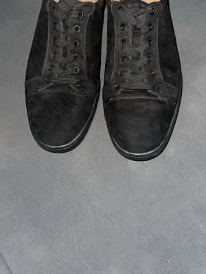 Christian Louboutin Louis Junior Suede Sneakers - Säljer ett par Christian Louboutin Louis Junior mocka Sneakers i svart mocka, storlek 43. Skorna är använda men ovandelen är fortfarande i bra skick. Det finns slitage och skrapmärken på de röda sulorna undertill, vilket syns på bilderna, men inget som påverkar användningen. Bekväma och stilrena designersneakers.