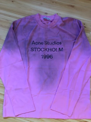 Rosa långärmad topp Acne Studios - Cool rosa långärmad topp från Acne Studios med tryck 'Acne Studios STOCKHOLM 1996' på bröstet. Rund halsringning och relaxed fit. Perfekt för dig som gillar streetwear och vill sticka ut lite extra.