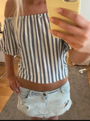 Randig offshoulder topp  - Snygg offshoulder topp med blå och vita vertikala ränder. Modellen är croppad och har korta, vida ärmar. Perfekt för varma dagar och ger en fräsch sommarkänsla. Tillverkad i lätt och luftig bomull.