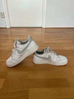 Nike Air Force 1 Sneakers - Storlek 41 - Säljer ett par Nike Air Force 1 i stilren vit/grå färg, storlek 41. Skorna är använda men i bra skick med normalt slitage. Ovandelen är välbevarad och sulorna har fortfarande gott om liv kvar. Perfekta som vardagsskor tack vare den klassiska designen som passar till de flesta outfits.
