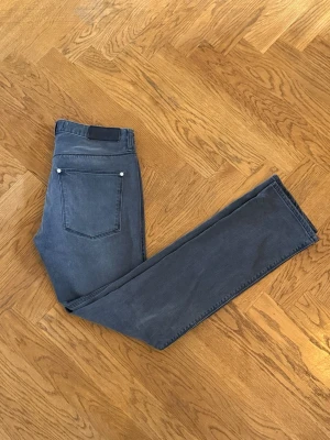 Acne Jeans - Säljer ett par grå jeans från Acne med raka ben och klassisk femficksmodell. Jeansen har diskreta slitningar framtill och silverfärgade nitar. Perfekta för en clean och stilren look. Materialet är mjukt denim i bomull.