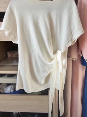 Vit topp med knyt i sidan - Säljer en vit topp med korta ärmar och snygg knytning i sidan. Toppen har en avslappnad passform och är tillverkad i mjukt bomullsmaterial. Perfekt att styla med jeans eller kjol för en enkel men trendig look.