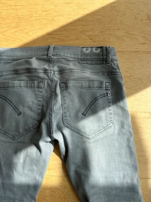 Dondup jeans  - Säljer ett par gråa skinny jeans från dondup  med klassiska bakfickor och diskret logga vid linningen. Jeansen har smal passform och är tillverkade i mjukt denimtyg som sitter snyggt. Perfekta för dig som gillar en clean och stilren look.